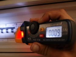 Mini pinza amperometrica PCE-DC3 misurando la corrente di un sootoquadro elettrica nella scurità.
